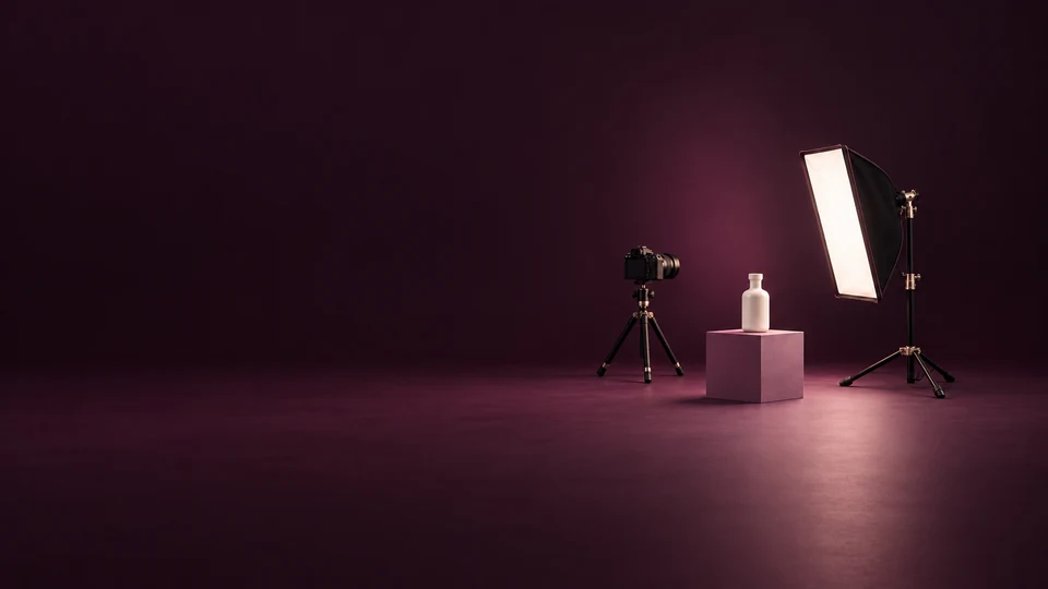 A camera on a tripod, an ivory bottle on a mauve plinth and a studio softbox.