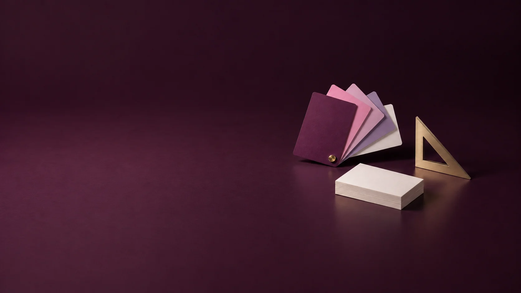 A fan of rose and plum colour cards beside an ivory card stack and metal set square.