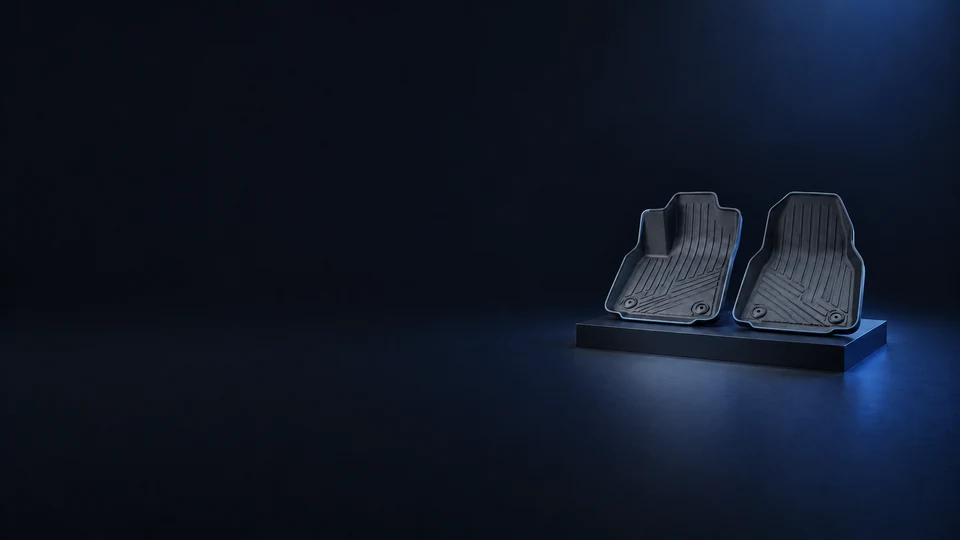 Two graphite rubber footwell liners with raised edges and channels on a low dark platform.