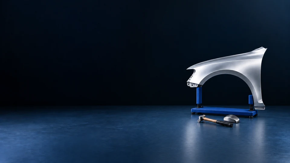 A complete silver automotive fender on a padded blue stand, with a bodywork hammer and steel dolly.