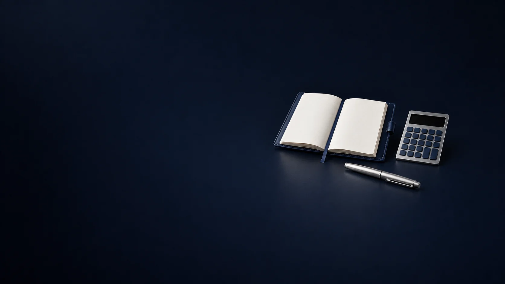 An open blank navy ledger beside an unmarked calculator and a capped silver pen.