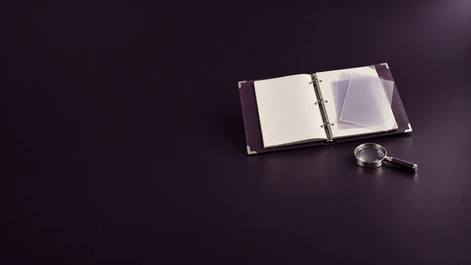 An open purple report binder with blank pages, translucent overlays and a silver magnifying glass.