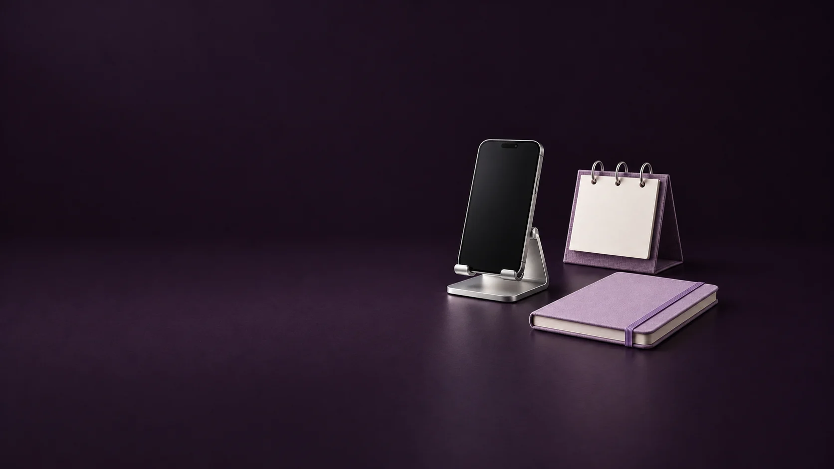 An inactive phone on a silver stand beside a blank violet desk calendar and lavender notebook.