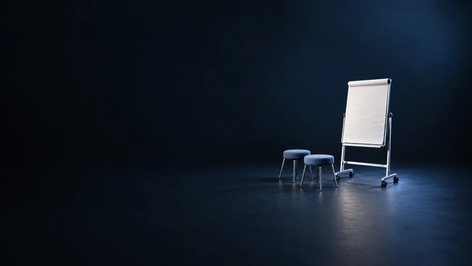 A blank flipchart on a wheeled metal easel beside two blue upholstered stools.