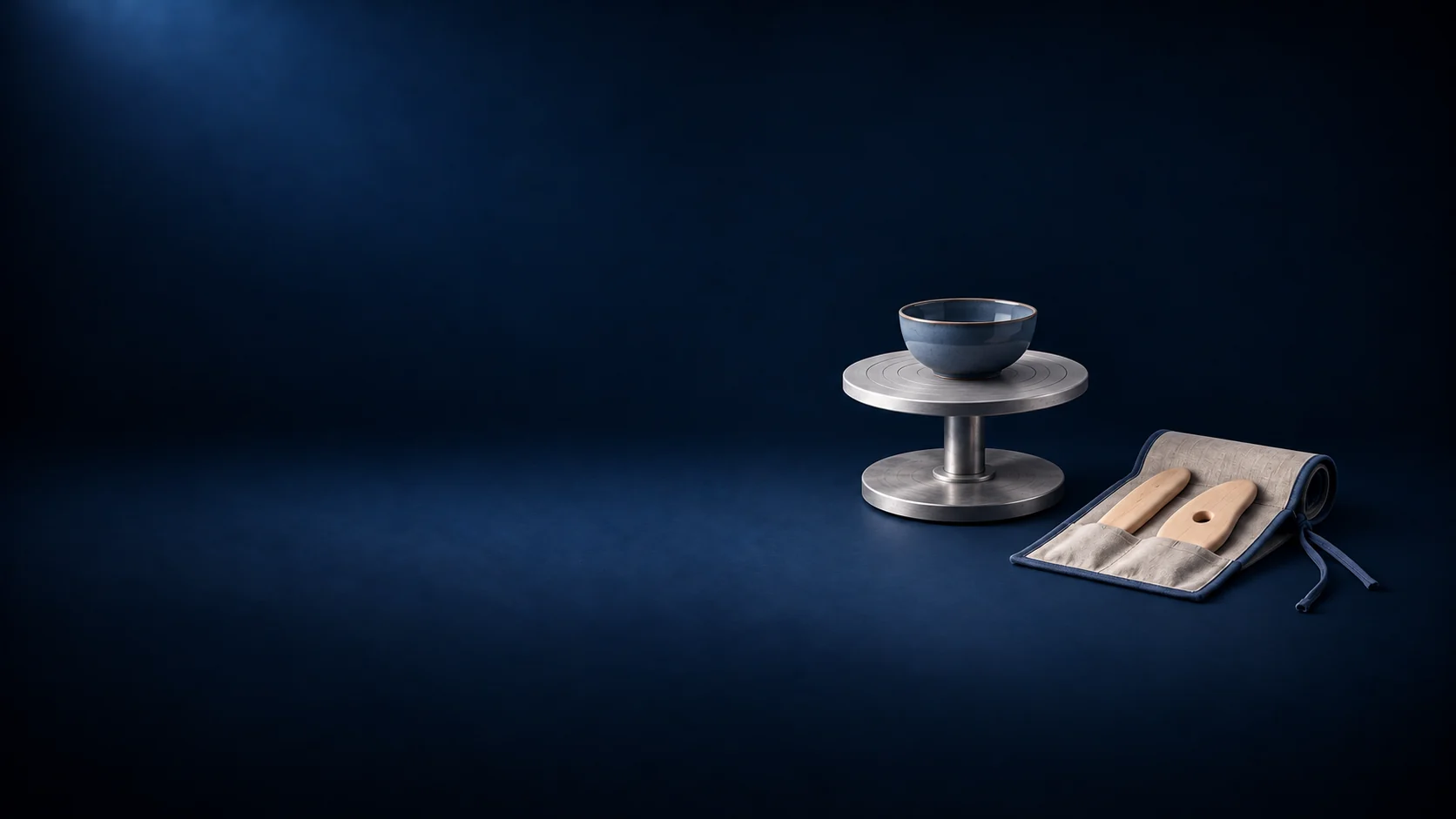 A blue bowl on a short metal banding stand beside a linen roll holding two wooden pottery ribs.