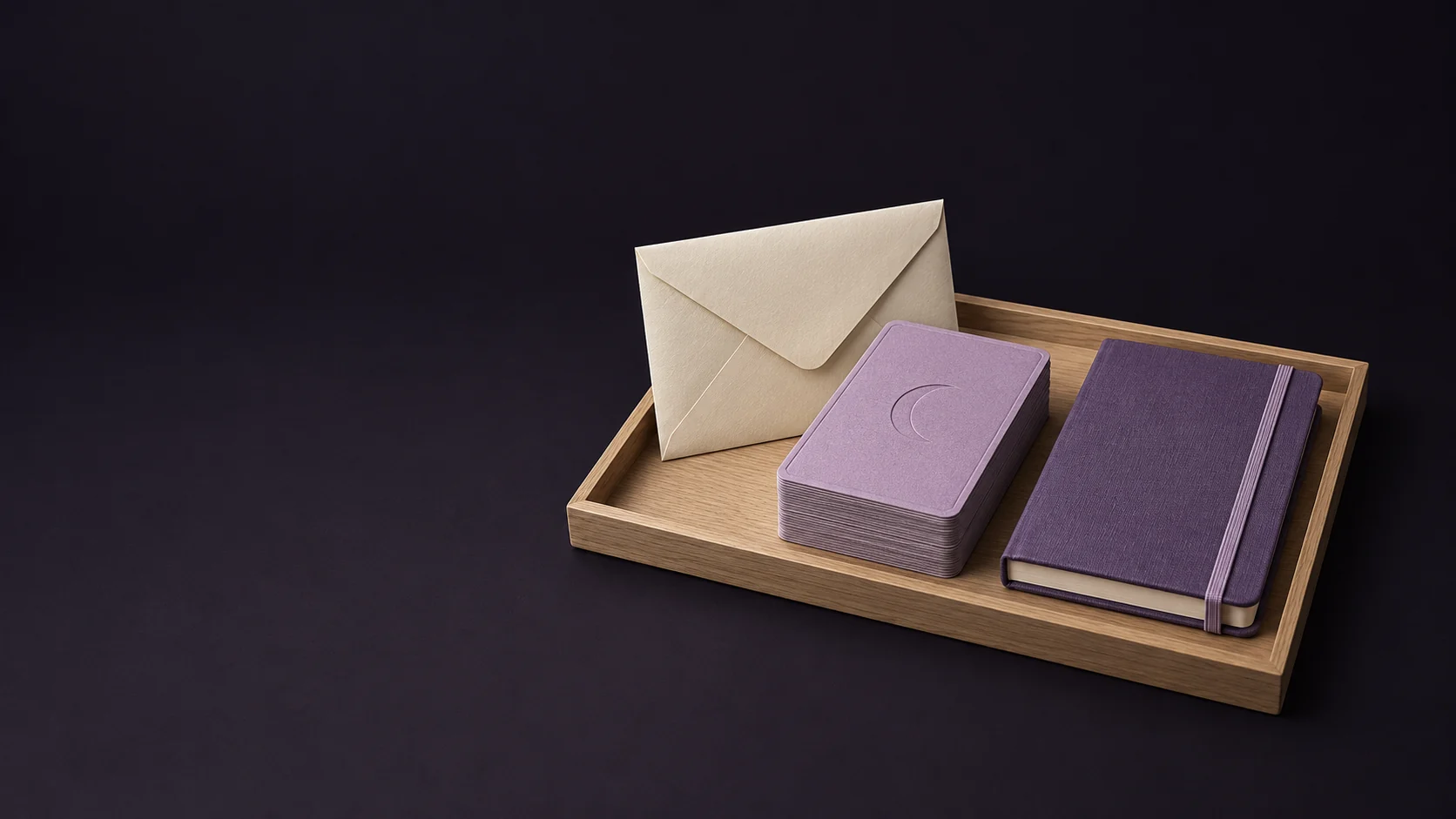 A mauve card deck with plain crescent backs beside a blank ivory envelope and amethyst practice notebook in an oak tray.
