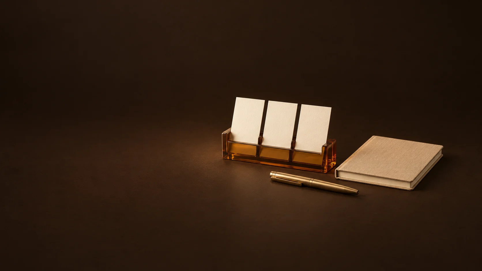 Three blank appointment cards in an amber holder beside a camel notebook and brass pen.