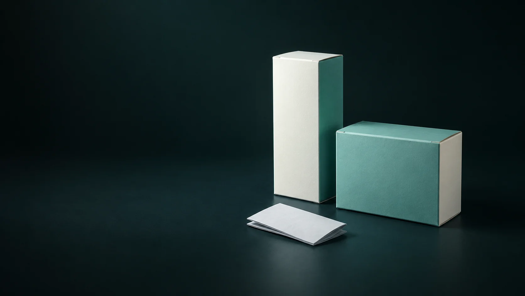 Two blank cartons of different proportions beside a folded ivory leaflet.