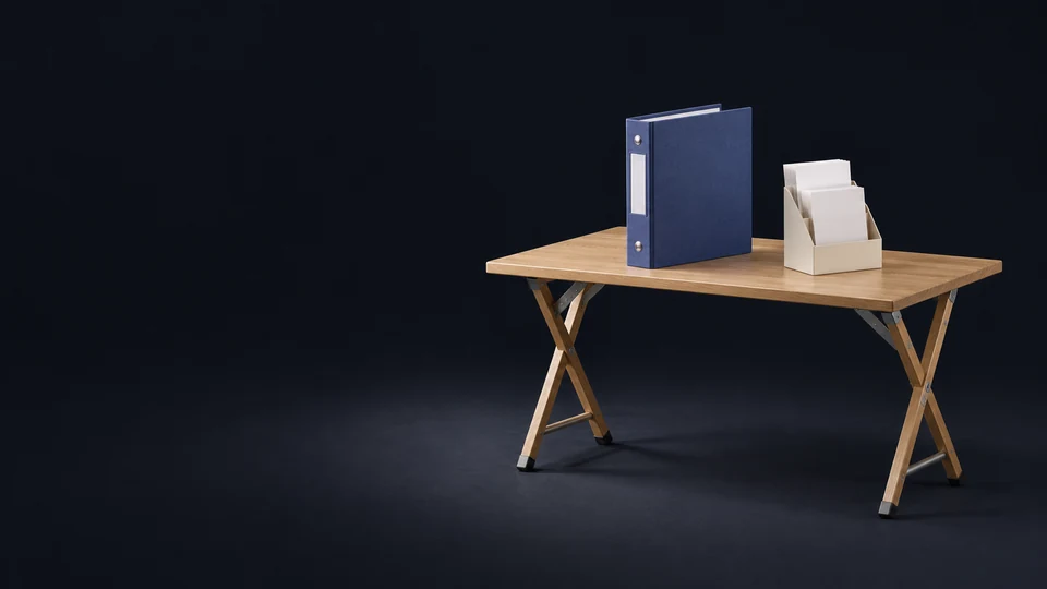 An oak trestle information table with an unmarked indigo docket binder and ivory rack of blank folded brochures.