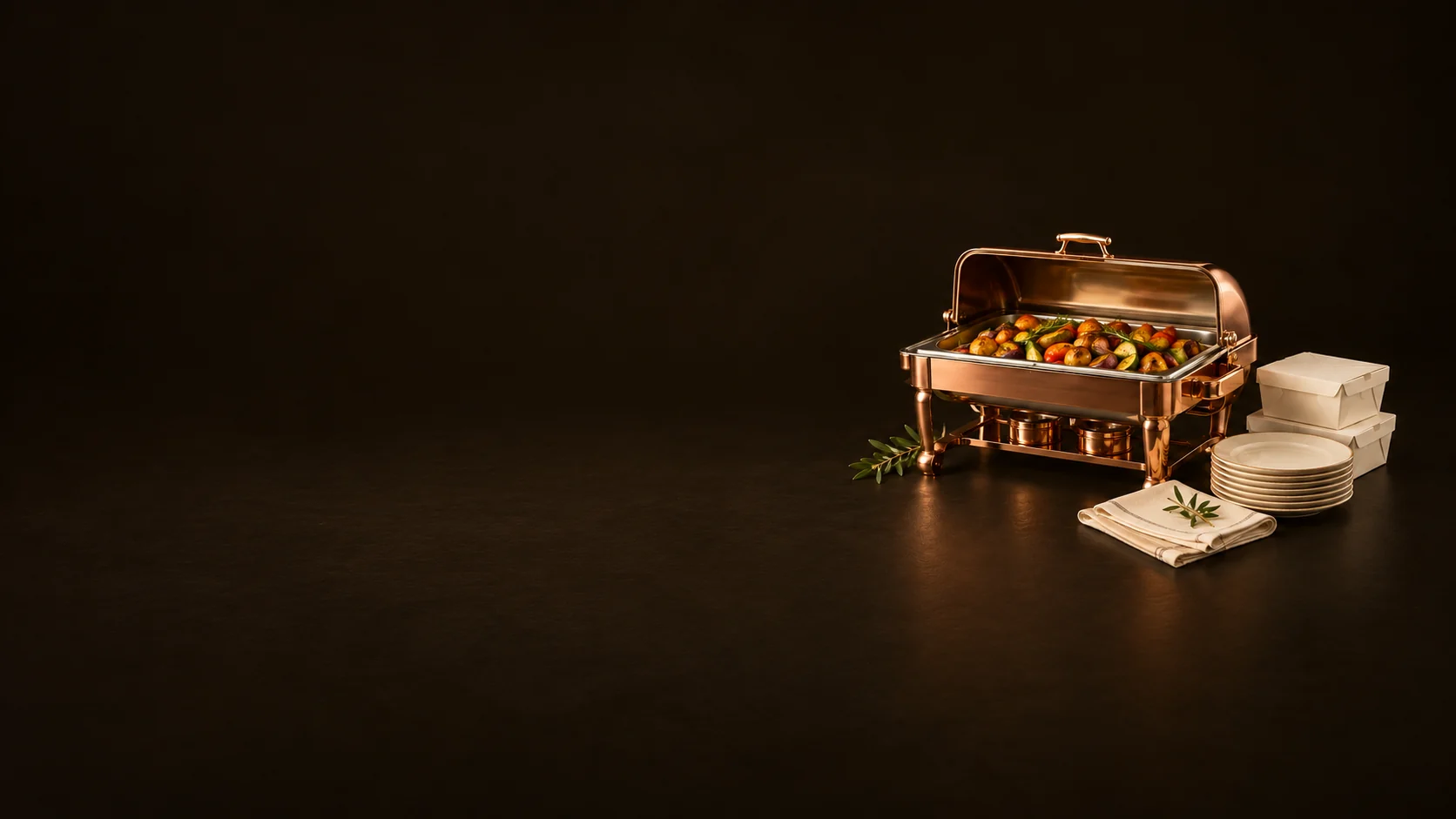 Copper catering dish with its lid raised over roasted vegetables, beside meal boxes, plates and folded linen.